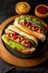 Homemade hot dogs with sausage, green salad, cucumber and red onion on the black background close up vertical photo