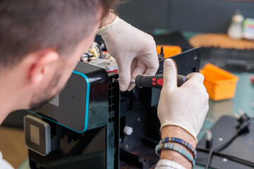 vista molto dettagliata sulla testa e le mani, coperte da dei guanti in lattice, di un giovane uomo italiano girato di spalle, mentre esegue dei lavori di manutenzione ad un apparecchio elettronico