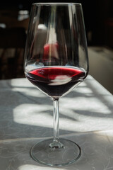 vista dettagliata di un calice, visto frontalmente e da vicino, riempito parzialmente con del vino rosso ed appoggiato su un tavolo coperto da una tovaglia bianca