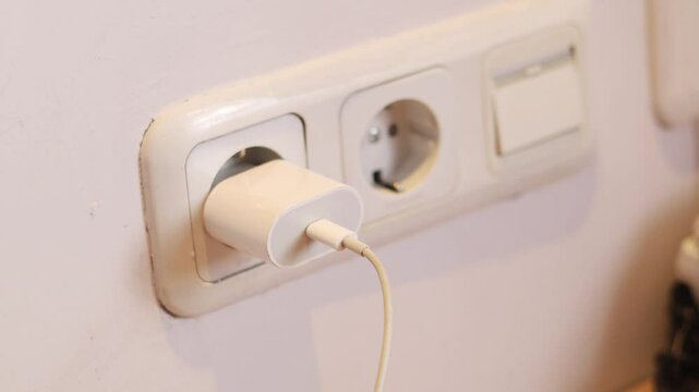 A hand pugging in a mobile phone charger into the wall power socket