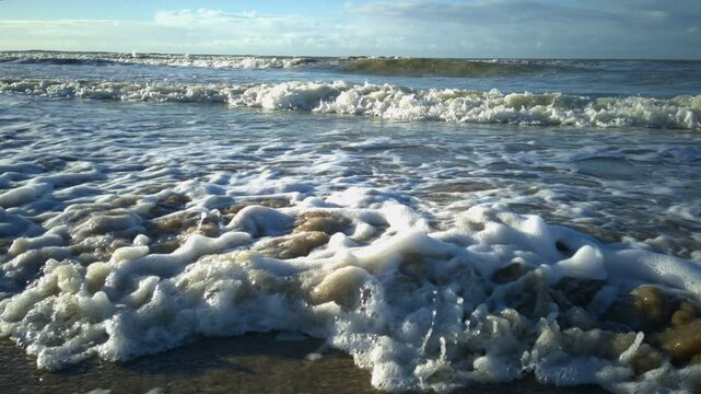 Close wide angle view on waves rolling on the beach on a synny autumnal day from a low position with no people