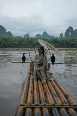 Hanfu girl with umbrella on bamboo raft in Xingping posing with cormorants