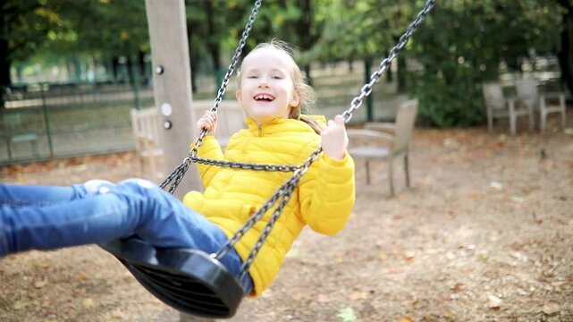 Happy 6 years old girl on a swing. Happy kid on playground swinging on seesaw. Outdoor autumn activities for children.