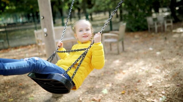 Happy 6 years old girl on a swing. Happy kid on playground swinging on seesaw. Outdoor autumn activities for children.