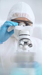 Scientist in ppe analyzing samples with microscope. Close-up of a focused researcher in a lab coat...