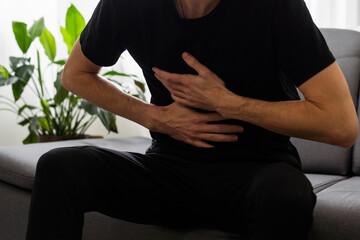 Man suffering stomach ache sitting on a couch in the living room at home