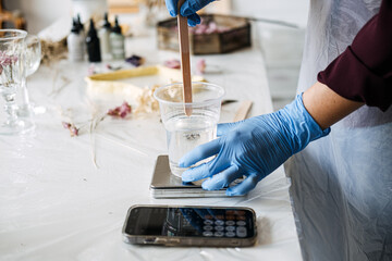 Close-up of hands mixing resin for DIY art project, wearing blue gloves and apron. Creative hobby,...