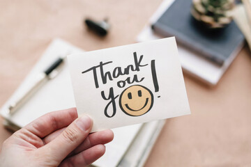 hand holding a handwritten thank you note with a smiley face drawn on it