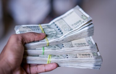 a hand holds multiple bundles of ₹500 Indian rupee notes, neatly stacked and tied with rubber bands, showcasing financial abundance and control over wealth. 