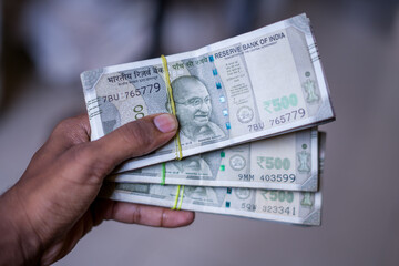 a hand holds multiple bundles of ₹500 Indian rupee notes, neatly stacked and tied with rubber bands, showcasing financial abundance and control over wealth. 