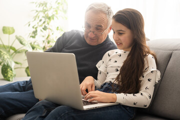 Happy retirement grandfather and pretty granddaughter laughing while watching e-book for learning...