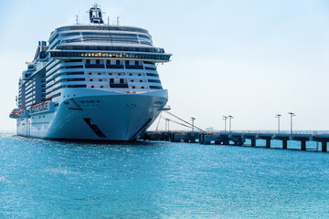 Naklejka premium A large cruise ship is docked at a pier. Only blue ocean and sky are visible. Travel destination and vacation theme