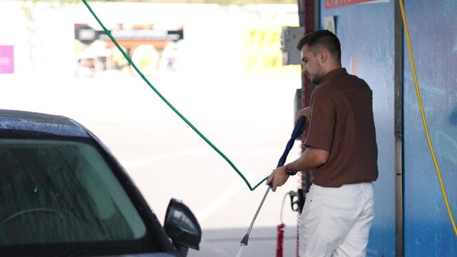 Handsome man washes his luxury car at a self-service car wash. Water under pressure