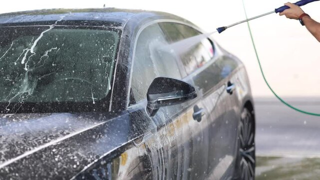 Handsome man washes his luxury car at a self-service car wash. Water under pressure
