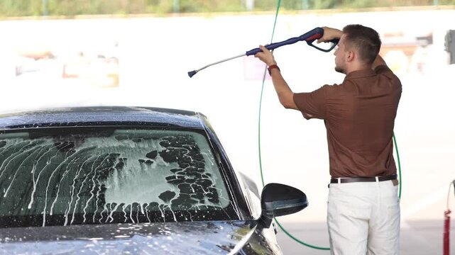 Side view of young man cleaning his car with a jet sprayer. Self service car washing