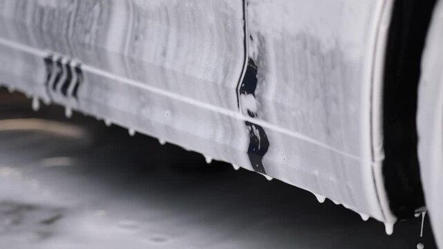 A luxury car covered in white foam at a self-service car wash, waiting. The foam is running down of the car. Close up view