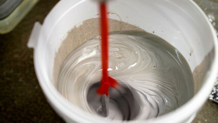 Construction worker mixing cement in a bucket with a red electric mixer