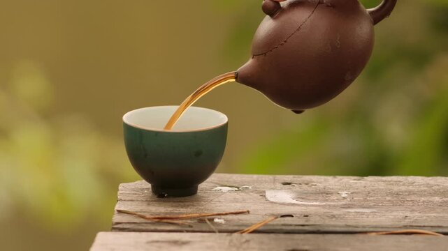 Close-up clay teapot pouring black tea into cup on Wooden Surface Outdoors