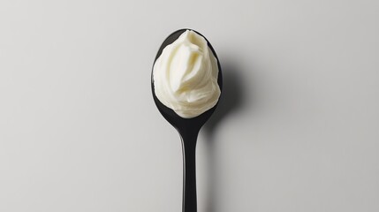 Top view of a spoon filled with creamy sour cream, isolated on a white background. 