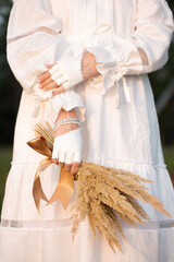 A woman in a white vintage dress and white leather mittens holds a bouquet of dried flowers