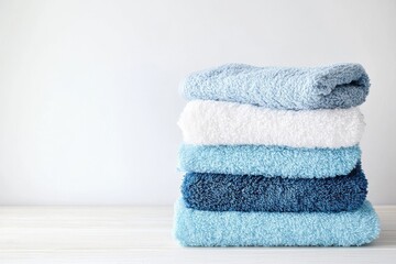 A neat stack of fluffy towels in shades of blue and white is placed on a light wooden surface