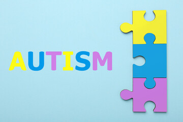 Autism word and colorful puzzle pieces on light blue background, top view