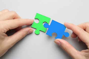 Woman joining puzzle pieces on light grey background, top view. Autism concept