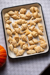 Small croissants and cookies in the shape of cats from puff pastry in a white baking dish, next to a pumpkin