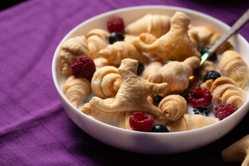 A breakfast of small croissants and cookies in the shape of a cat with fresh berries and milk. Halloween breakfast concept