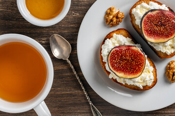 Two sandwiches with fresh fig slices, white cottage cheese, honey and walnuts on toast bread on a plate, top view, closeup. Healthy eating. Delicious breakfast, lunch or snack