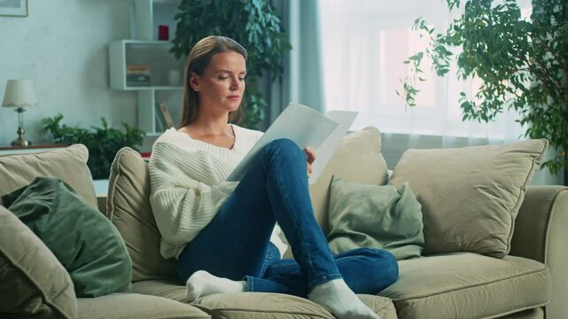 Montage showcases a young woman reviewing paperwork while relaxing on a sofa in a cozy living room. Slow motion captures her focused and thoughtful demeanor during the process