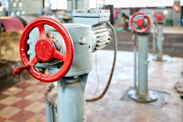 Row of old retro Motor drive electric valve wheels painted red selective focus with extension device over out of focus background tiled floor and perforated metal sheet stamping plates with copyspace.