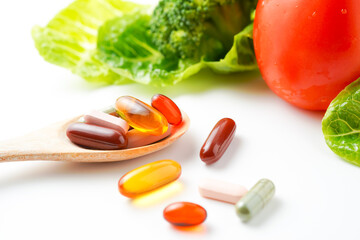 Wooden spoon with herbal pills capsules, dietary supplements vitamins on vegetables background