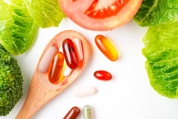 Pills and capsules in wooden spoon with fresh vegetables, Multivitamins and supplement
