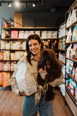 Beautiful young woman enjoying in modern pet shop together with her adorable brown toy poodle.