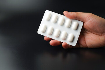 hand holding pills Medicine tablet capsules in blister pack on a black background