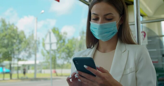 Young woman in protective medical face mask in a public transport using smartphone. Young girl usig app on a smartphone.
