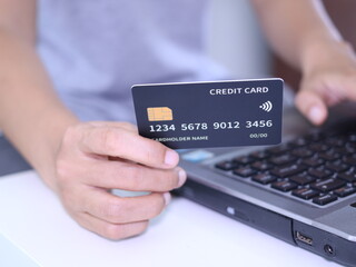 Hand hold black credit card front of the laptop.