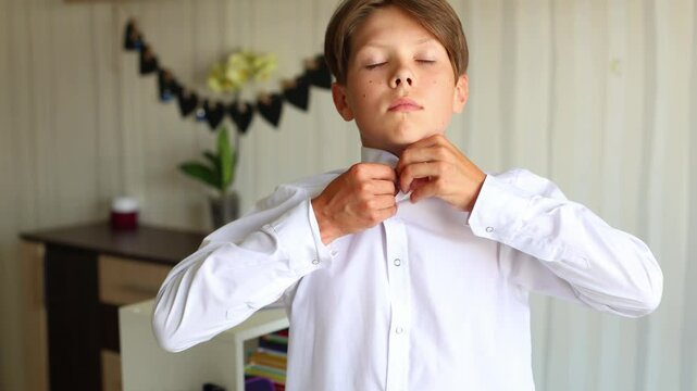 a teenage boy is shown in a close up as he prepares to wear a white school shirt. He carefully unbuttons the shirt and slides it over his arms. Moment in a teenager daily life
