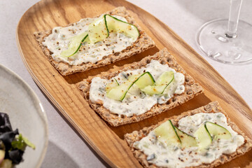 Wholegrain toast with tsasiki greek souce and cucumber on wooden plate in sunny atmosphere