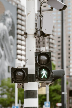A city street crosswalk signal is lit green, allowing pedestrians to cross safely amidst urban structures, highlighting pedestrian safety in busy environments.