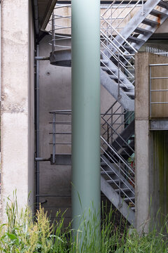 A mix of concrete and metal elements form an industrial staircase, suggesting functionality and contrast between urban design and surrounding natural foliage.