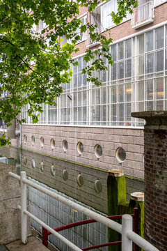 A brick industrial building with large windows sits beside water, capturing reflections and bringing together elements of industry, nature, and architectural charm in Rotterdam