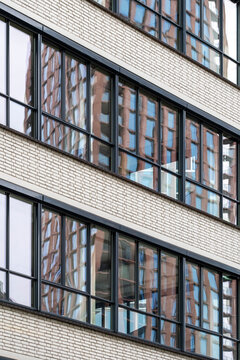 A contemporary building facade boasts rows of reflective glass windows, epitomizing urban elegance, symmetry, and modern architectural design efficiency.