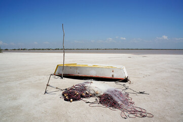 An old wooden boat rests on the shore, with tangled fishing nets draped over its sides. Its...
