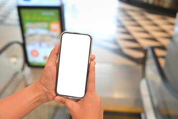 Close up woman holding smartphone while standing on escalator in a shopping mall