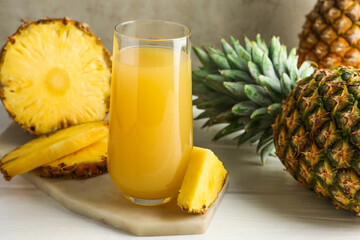 Tasty pineapple juice in glass and fresh fruits on white wooden table against grey background, closeup