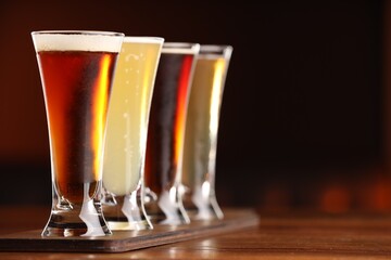 Glasses with different types of beer on wooden table against color background, closeup. Space for text