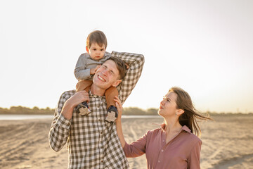 Happy family walking on the road in the park. Father, mother holding baby son on hands and going together. Rear view. Family Ties concept.