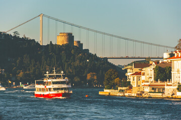 Ferry sailing on the Bosphorus under Fatih Sultan Mehmet Bridge in Istanbul, with Rumeli Fortress...
